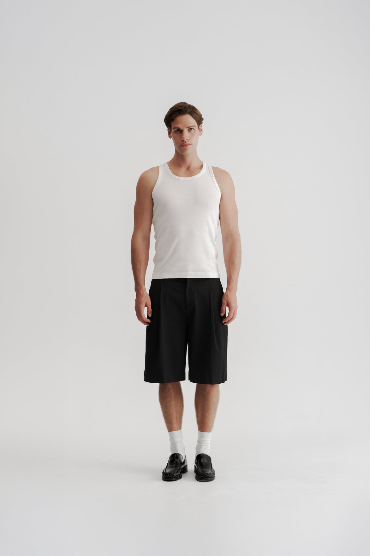 Full-length front view of a model wearing Black Pleated Shorts, showing the wide fit and below-knee length.
