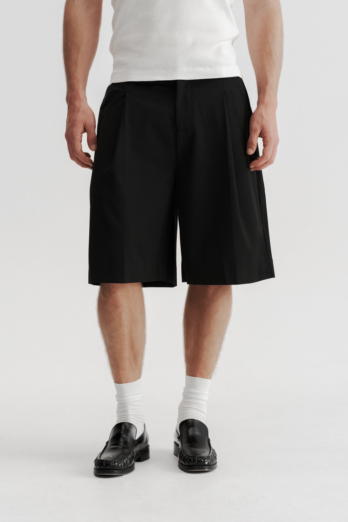Front view of a model wearing Black Pleated Shorts, showing the deep pleats and wide legs.