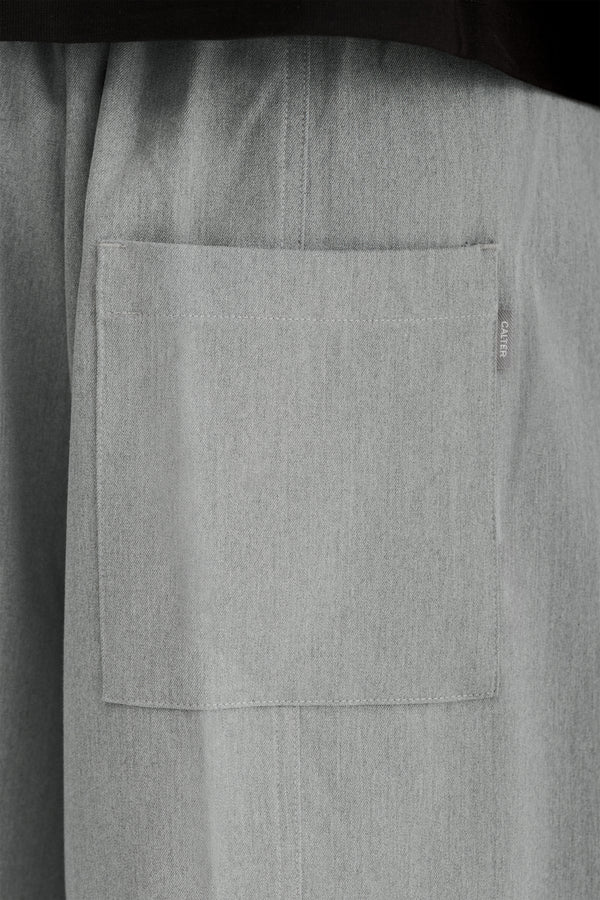 Close-up of a rear patch pocket and woven CALTER label on Grey Pleated Shorts.