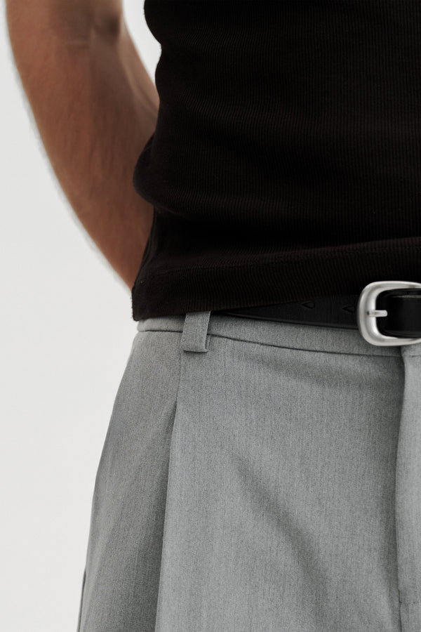 Close-up of the waistband, belt loop and front pleat of Grey Pleated Shorts worn with a black belt.