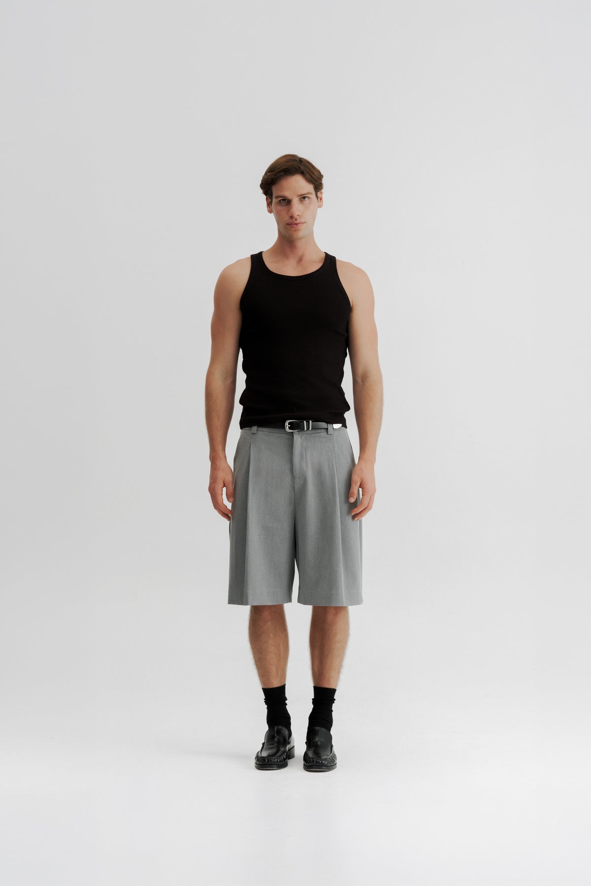 Full-length front view of a model wearing Grey Pleated Shorts, showing the wide fit and below-knee length.