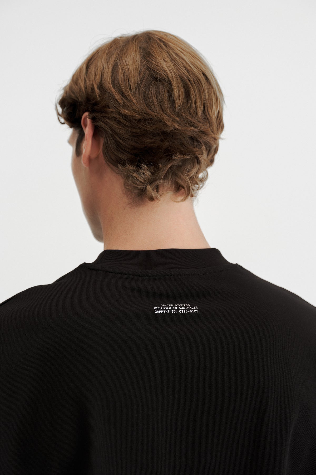 Close-up of the white garment ID print below the rear neckline of the Black Stamp Tee.