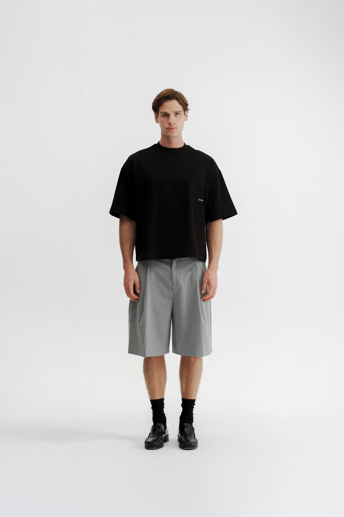 Full-length front view of a model wearing the Black Stamp Tee with Grey Pleated Shorts.