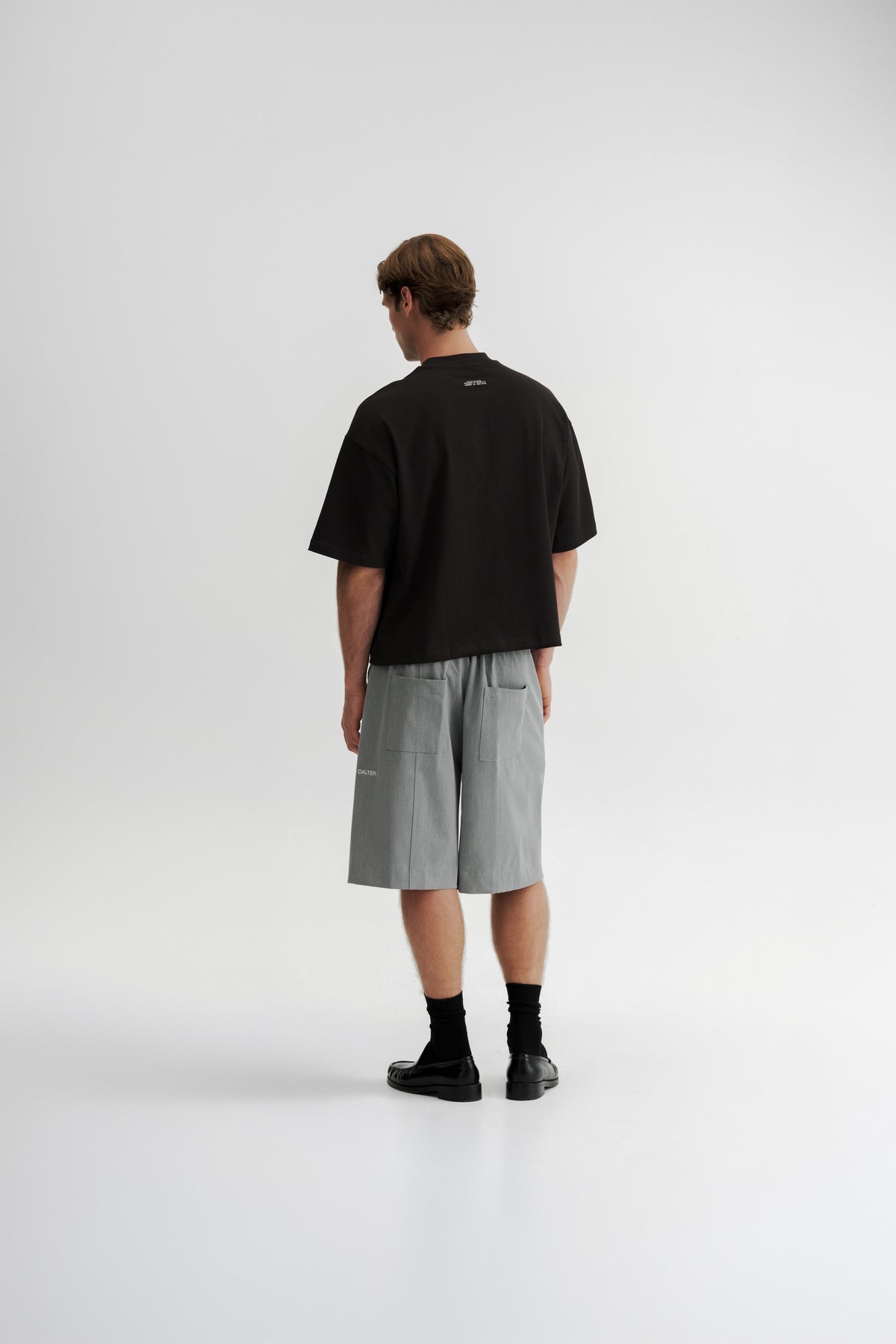 Rear view of a model wearing the Black Stamp Tee, showing the wide fit and garment ID print below the neckline.