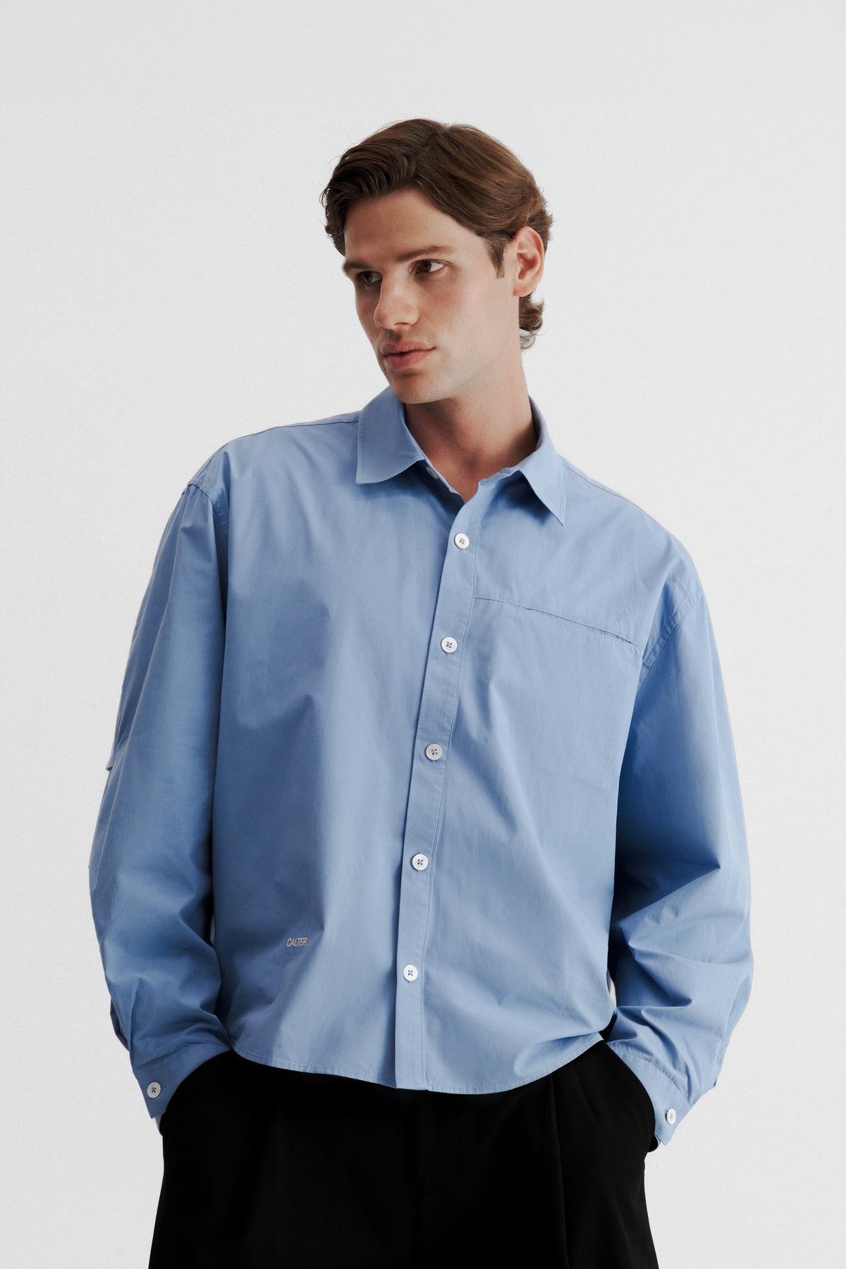 Model wearing the Technical Blue Pleated Shirt buttoned, showing its wide body and hidden chest pocket.