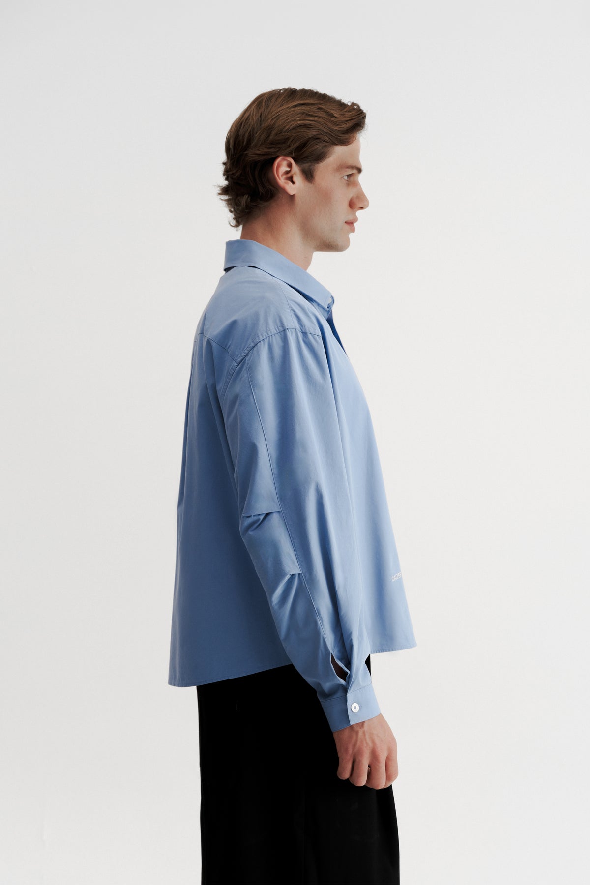 Side view of a model wearing the Technical Blue Pleated Shirt, showing the elbow pleats and shaped sleeve.