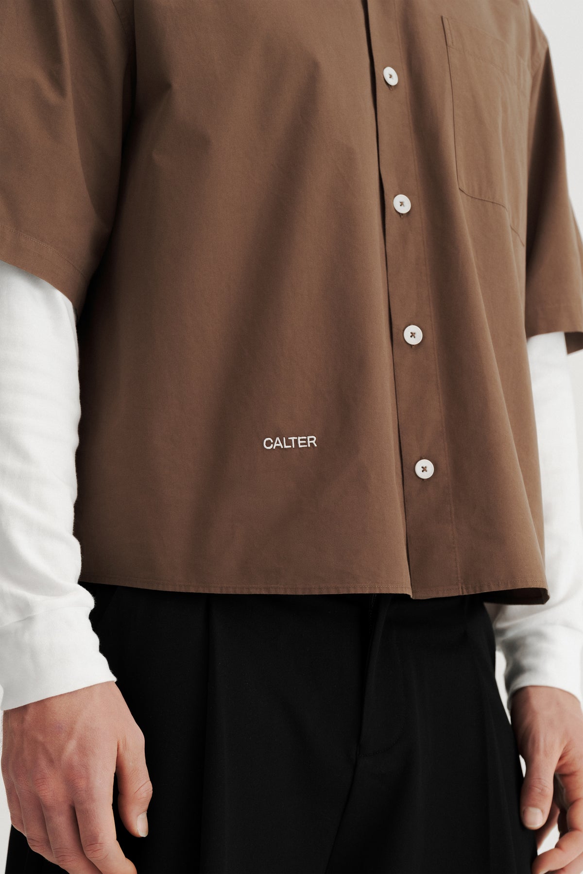 Close-up of the buttons, chest patch pocket and CALTER embroidery near the front hem of the Brown Volume Shirt.
