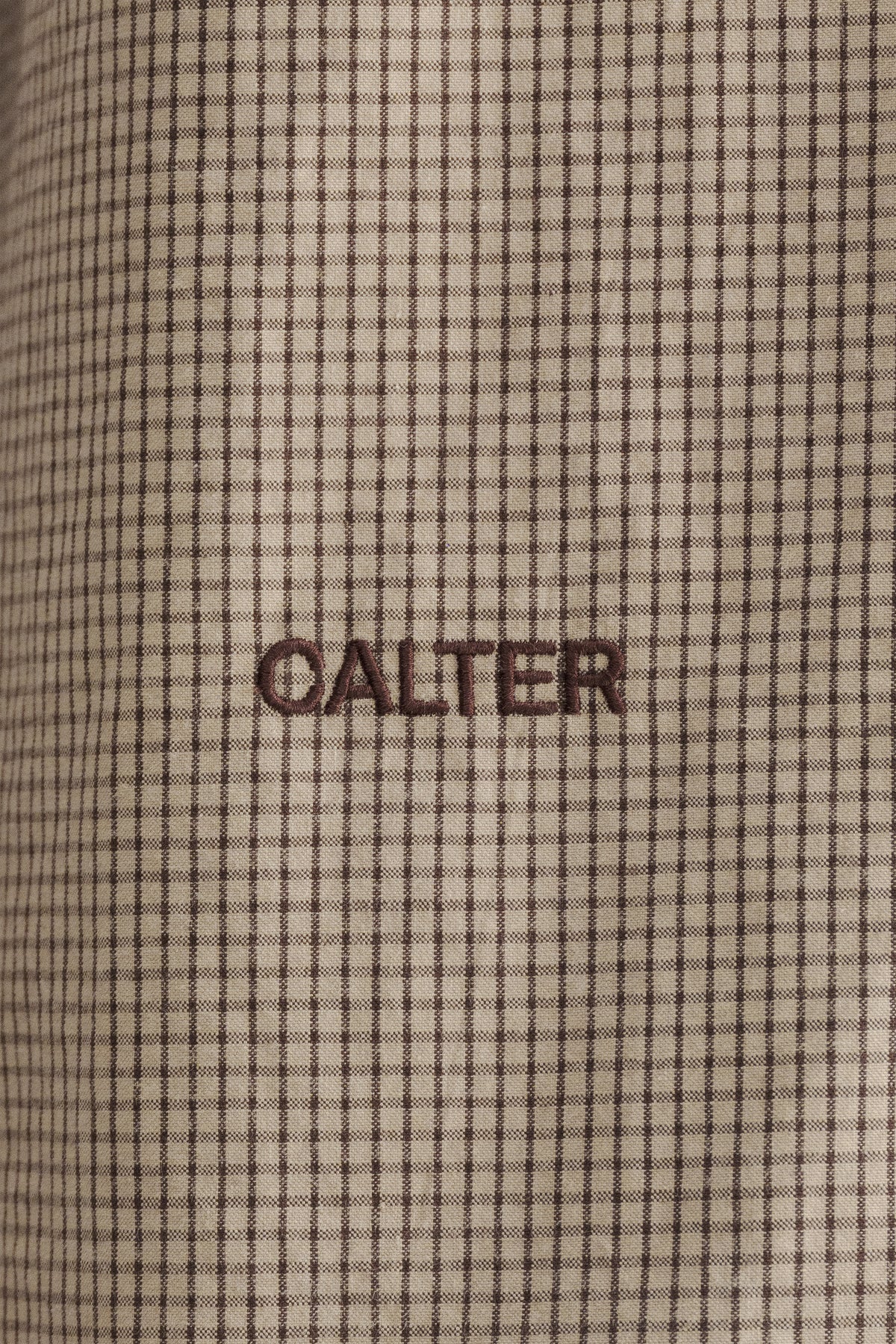 Close-up of the microcheck pattern and contrast CALTER embroidery on the Sand Microcheck Studio Shirt.