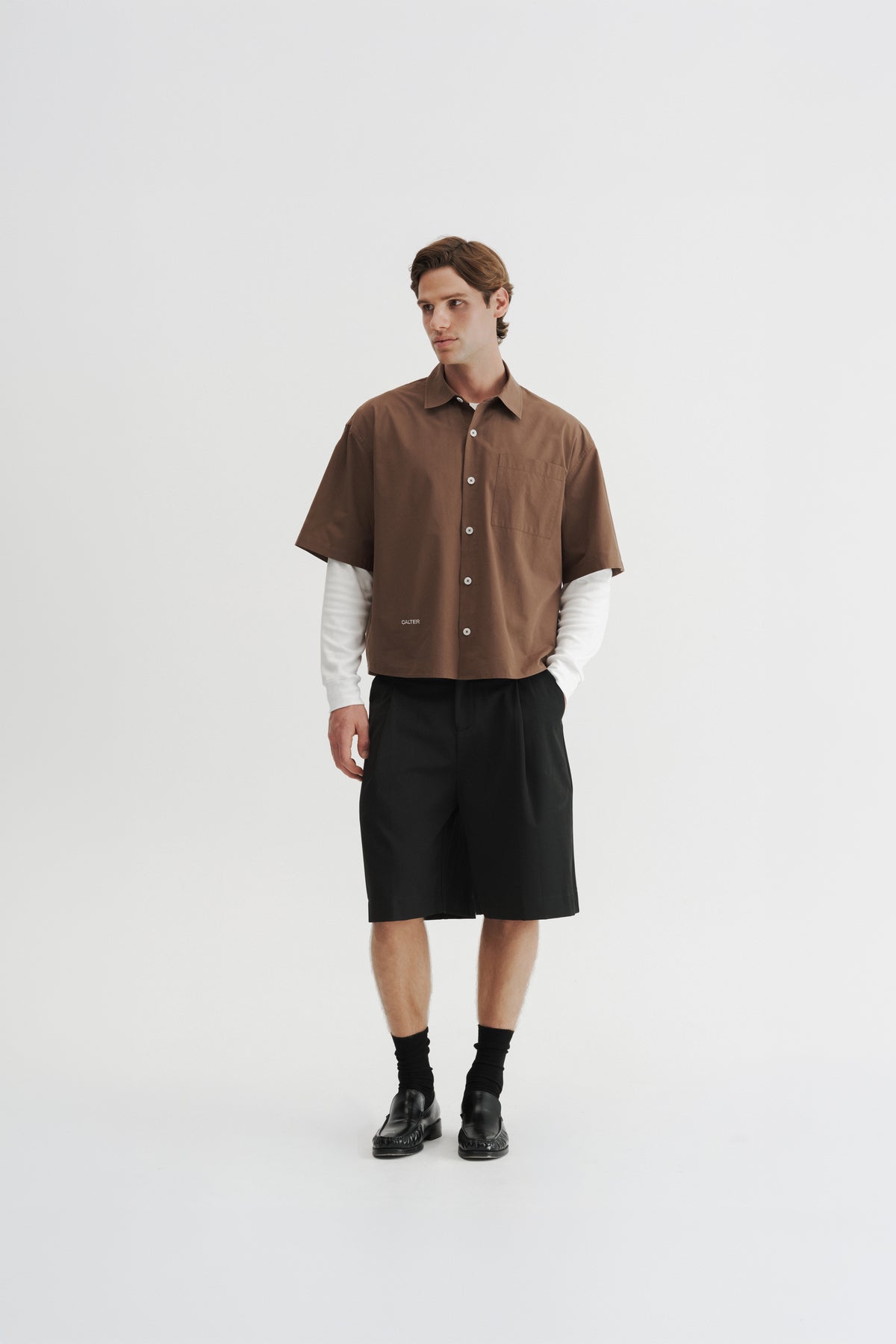 Three-quarter front view of a model wearing the Brown Volume Shirt with Black Pleated Shorts.