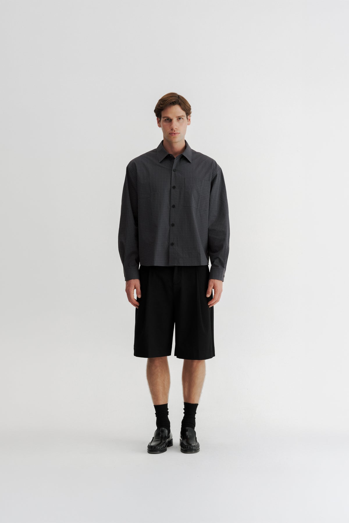 Full-length front view of a model wearing the Slate Microcheck Studio Shirt with Black Pleated Shorts.