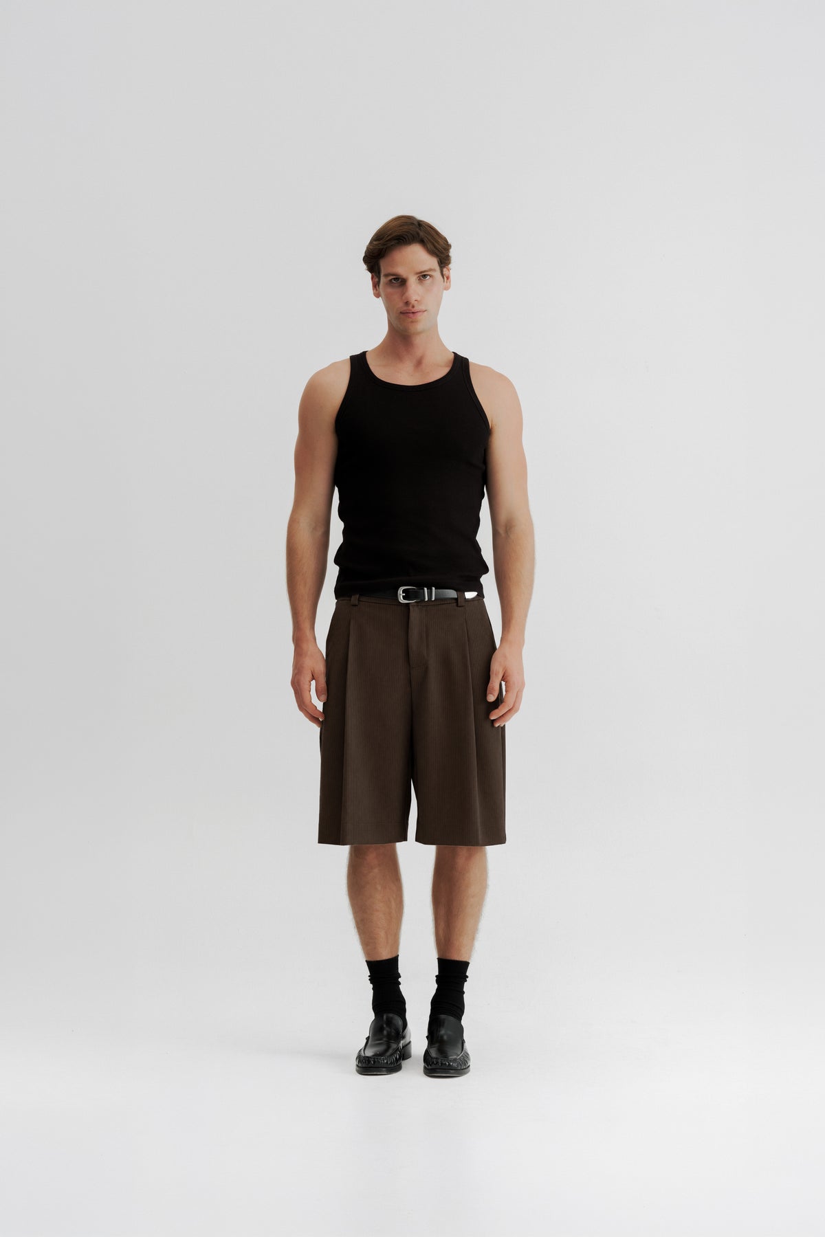 Full-length front view of a model wearing Brown Stripe Pleated Shorts, showing the wide fit and below-knee length.